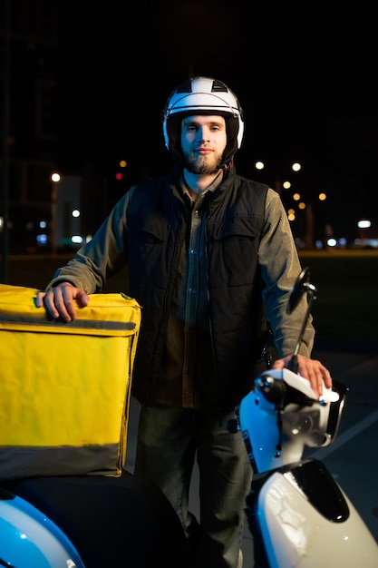 Avondportret van een mannelijke koerier op een scooter 24 uur per dag eten bezorgen tijdens de pandemie
