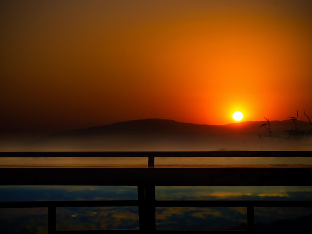 Avondschemering Goud met Mist en Silhouet Houten BalkonSchoonheid Zonlicht Oranje Wolk Hemel Natuur AchtergrondReflectie Horizon Zonsopgang met BerglandschapToerisme Vakantie Reizen Vakanties