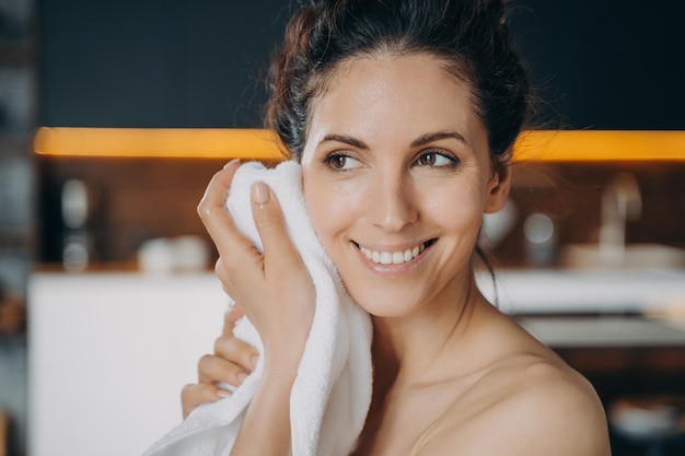 Avondschoonheidsroutine en hygiëne Kaukasische gelukkige vrouw veegt gezicht af met een handdoek na het wassen