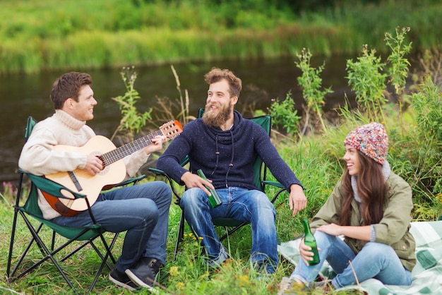 avontuur, reizen, toerisme en mensenconcept - groep glimlachende toeristen die gitaar spelen en bier drinken op de camping