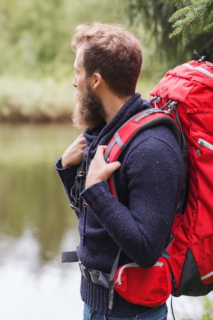 Foto avontuur, reizen, toerisme, wandelen en mensenconcept - glimlachende man met baard en rode rugzak wandelen