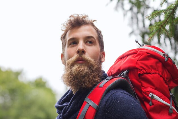 avontuur, reizen, toerisme, wandelen en mensenconcept - man met baard en rode rugzak wandelen