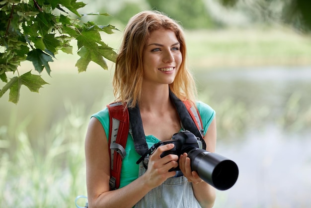 avontuur, reizen, toerisme, wandeling en mensenconcept - gelukkige jonge vrouw met rugzak en camera die buitenshuis fotografeert