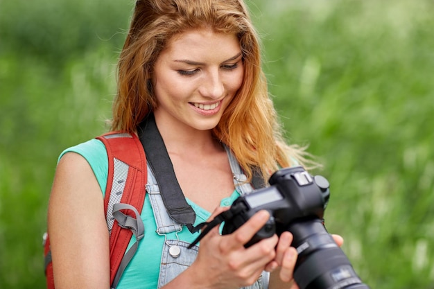 avontuur, reizen, toerisme, wandeling en mensenconcept - gelukkige jonge vrouw met rugzak en camera die buitenshuis fotografeert