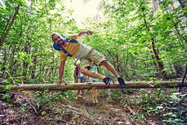 avontuur, reizen, toerisme, wandeling en mensenconcept - groep glimlachende vrienden die met rugzakken lopen en over omgevallen boomstam in bos springen