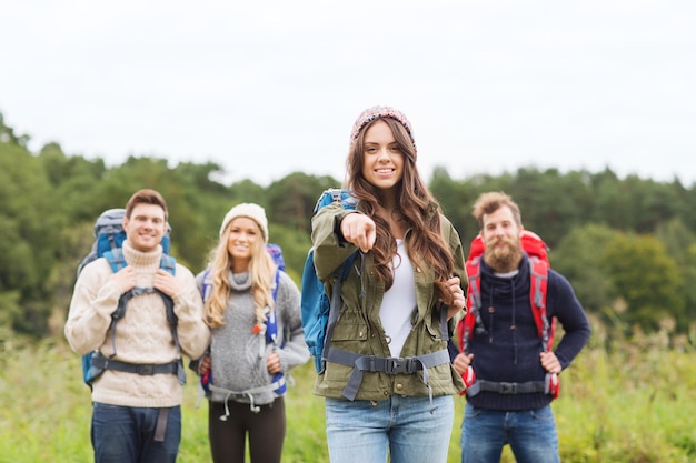 avontuur, reizen, toerisme, wandeling en mensenconcept - groep lachende vrienden met rugzakken die naar buiten wijzen