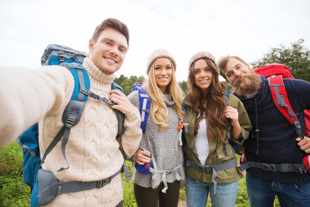 Foto avontuur, reizen, toerisme, wandeling en mensenconcept - groep lachende vrienden met rugzakken die selfie buitenshuis maken