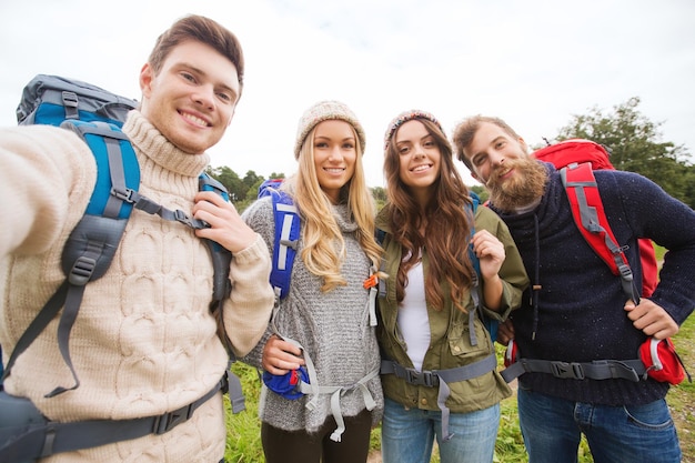 Foto avontuur, reizen, toerisme, wandeling en mensenconcept - groep lachende vrienden met rugzakken die selfie buitenshuis maken