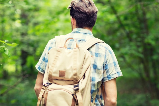 avontuur, reizen, toerisme, wandeling en mensenconcept - jonge man met rugzak die van achteren in het bos wandelt