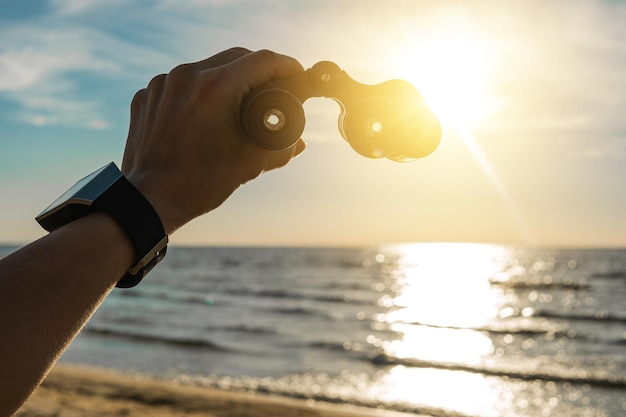 Avontuur vrouwelijke hand met een vintage verrekijker tegen fel zonlicht op prachtig strand met mooie blauwe lucht