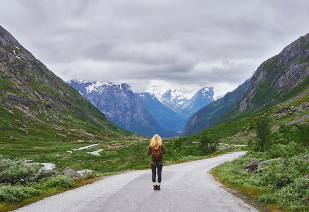 Avontuurlijke backpackende vrouw reist op de weg in epische majestueuze bergsneeuwlandschap