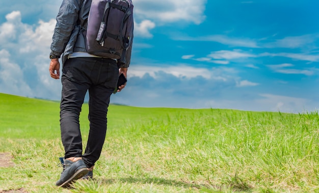 Avontuurlijke man in het veld, man met rugzak in het veld zijwaarts kijkend, close-up van stappen van een jonge backpacker