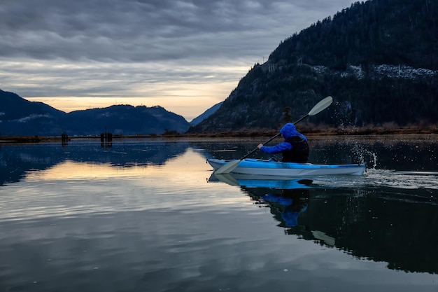 Avontuurlijke man kajakken in rustig water tijdens een bewolkte winterzonsondergang