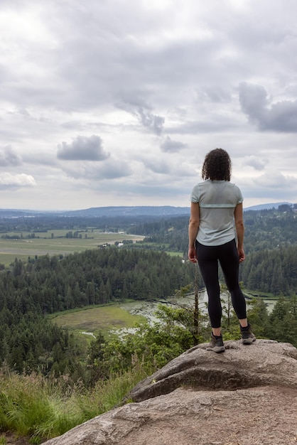 Avontuurlijke vrouw die op de top van een rots staat en uitkijkt over het canadese natuurlandschap