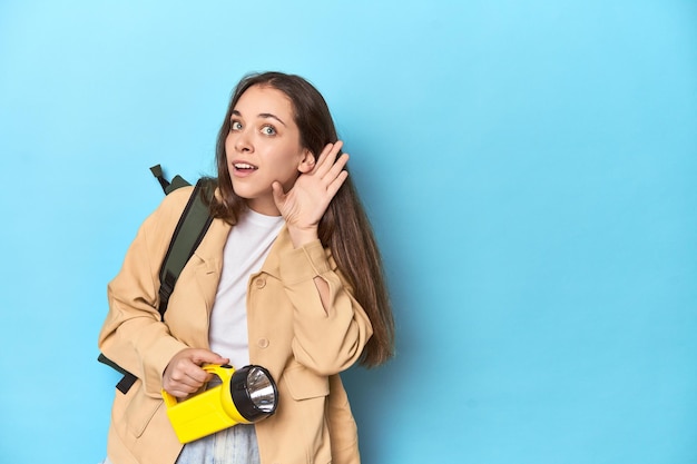 Avontuurlijke vrouw met zaklamp en rugzak klaar om te verkennen probeert te luisteren naar een roddel