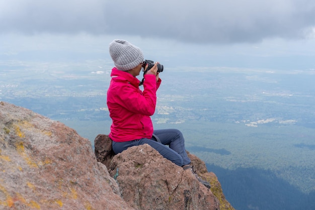 Avontuurlijke vrouwelijke fotograaf zittend op de rots tijdens het fotograferen van bergen