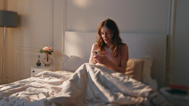 Photo awake woman typing phone in morning sunlight smiling calm girl resting in bed
