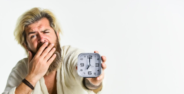 写真 覚醒のコンセプト不眠症睡眠障害健康的な習慣とライフスタイル睡眠に関する一般的な推奨事項ストレスを感じた男の目覚まし時計眠い男とベッドの目覚まし時計目覚まし時計を持つひげを生やした男