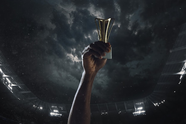 Award of victory, male hands tightening the cup of winners against cloudy dark sky