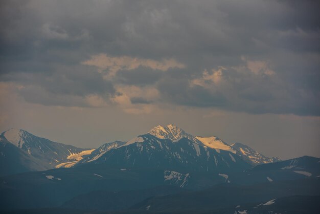 Awesome aerial view to high snow mountain peak in sunlight in overcast Atmospheric mountain landscape at high altitude with cloudiness Alpine view to snowy mountain top in light under cloudy sky