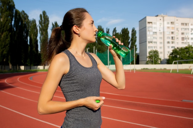 スタジアムでのランニング中に水を飲む素晴らしいブルネットの女性。テキスト用のスペース