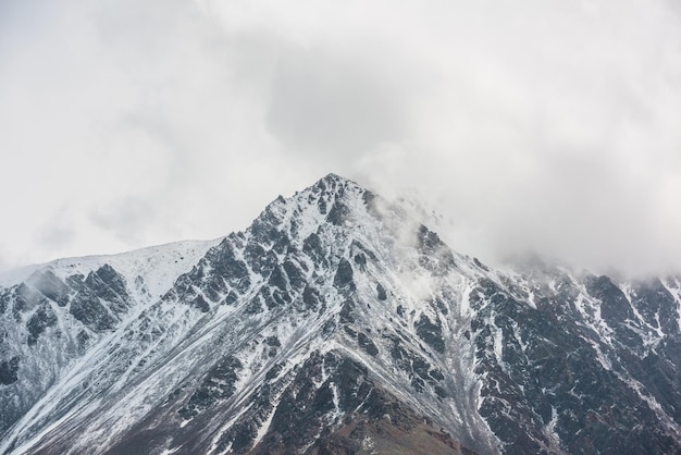 Fantastico paesaggio con un'alta montagna innevata che ha raggiunto la cima con rocce affilate in nuvole basse vista spettacolare sulla montagna innevata picco appuntito in un cielo poco nuvoloso