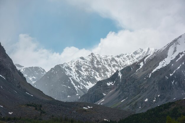 Удивительный пейзаж с высоким снежным горным хребтом с острыми скалами в облачном небе Драматический вид на снежные горы в переменчивую погоду Атмосферный горный пейзаж с белым снегом на черных скалах