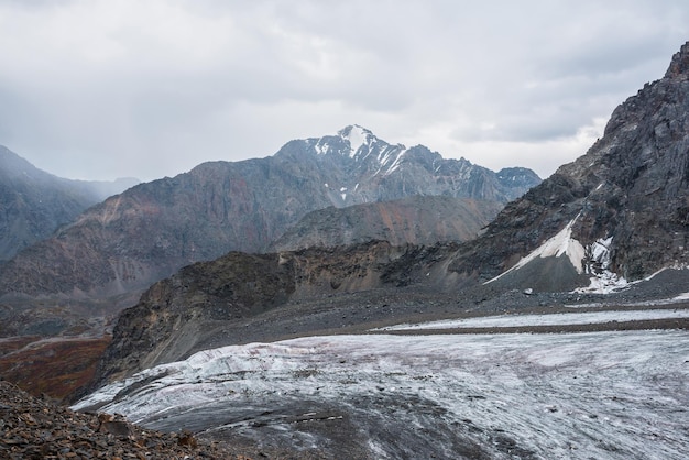 写真 氷河の長い舌と高い山脈の反対側にある素晴らしい風景 った天候でい岩の頂上 劇的ない空で円<unk>状の尖った頂上 い岩の間に大きな氷河.