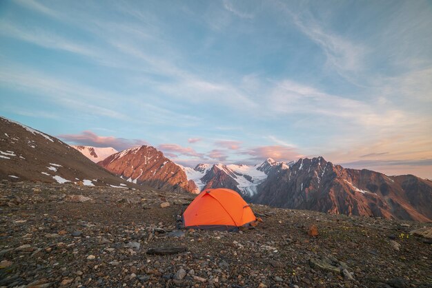 Awesome landscape with vivid orange tent with view to high snow mountains in sunrise colors Colorful scenery with sunlit gold rocks and mountains at sunrise Gold early morning at very high altitude