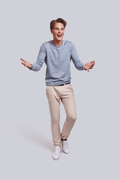 Awesome news! Full length of handsome young man keeping mouth open and gesturing while standing against grey background