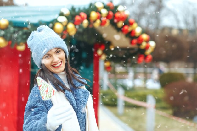 降雪時にクリスマスマーケットでキャンディーを保持している素晴らしい笑顔の女性。空きスペース