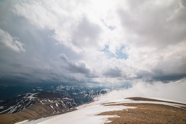 写真 雲を通して高い雪山までの素晴らしいトップビュー 低い雲の中に美しい雪山がある風光明媚な風景 石の丘から低い雲のある雪山脈までの雰囲気のある高山の景色