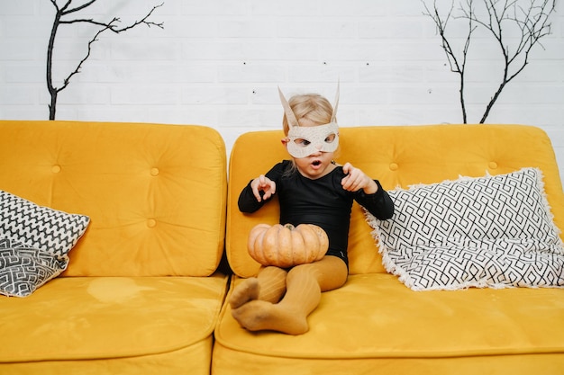 Awkward little girl in a mask dressed for halloween on a couch grimacing