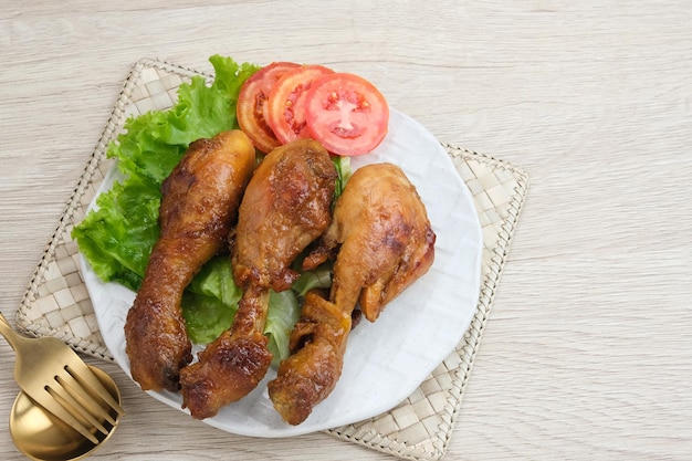 Ayam Bakar (gegrilde kip) met kruiden en specerijen. Geserveerd op een bord met sla en tomaten.