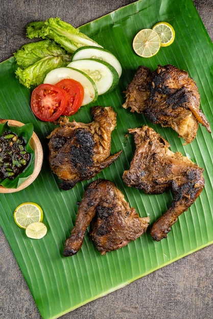 소박한 나무 배경에서 바나나 잎 촬영에 Ayam bakar 또는 구운 치킨