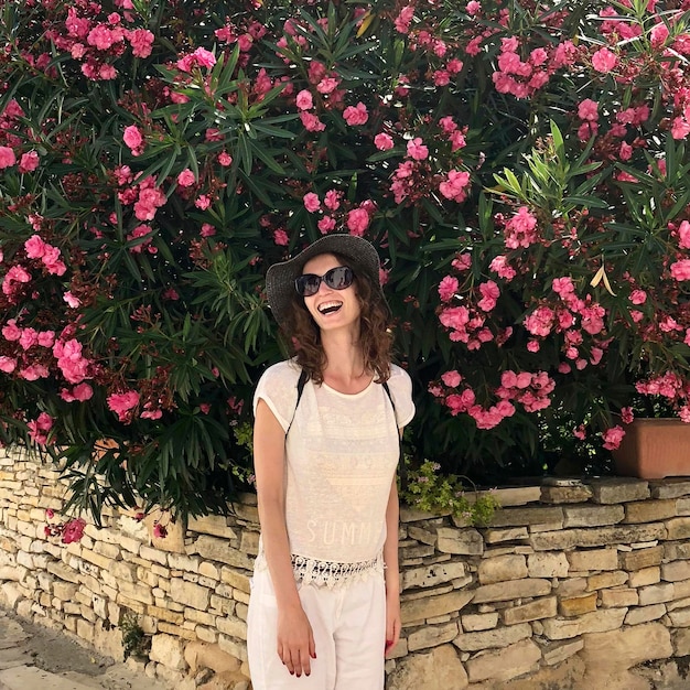 Ayia Napa Cyprus summer photo with beautiful happy woman stands in front of bush with pink flowers