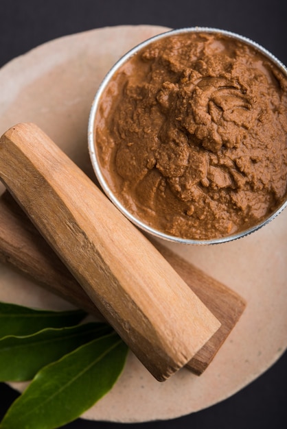 Photo ayurvedic chandan or sandalwood paste in silver bowl with sticksand leaves placed over sahanor sahana or circular stone base for creating paste