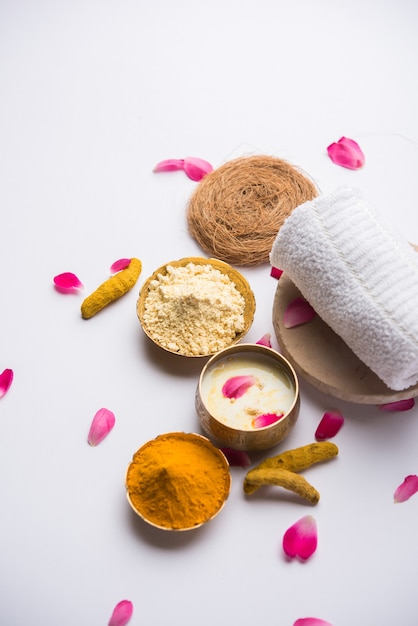 장미 꽃잎, 스크럽 및 흰색 냅킨이 있는 황동 그릇에 담긴 Gram Flouror besan, Haldi 및 우유 ubtan을 사용한 Ayurvedic 얼굴 팩 또는 마스크. 선택적 초점