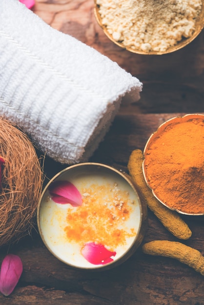 장미 꽃잎, 스크럽 및 흰색 냅킨이 있는 황동 그릇에 담긴 Gram Flouror besan, Haldi 및 우유 ubtan을 사용한 Ayurvedic 얼굴 팩 또는 마스크. 선택적 초점