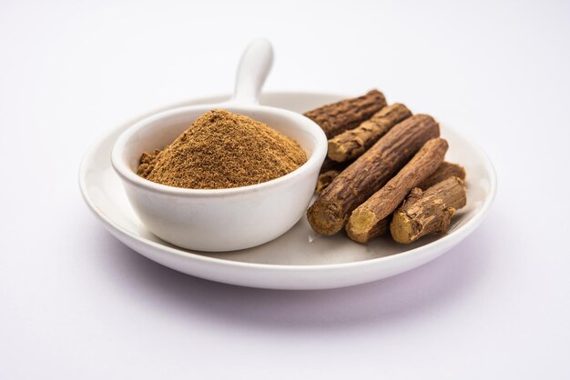 Ayurvedic Mulethi or Liquorice root stick or jeshthamadh powder served in a bowl over moody background