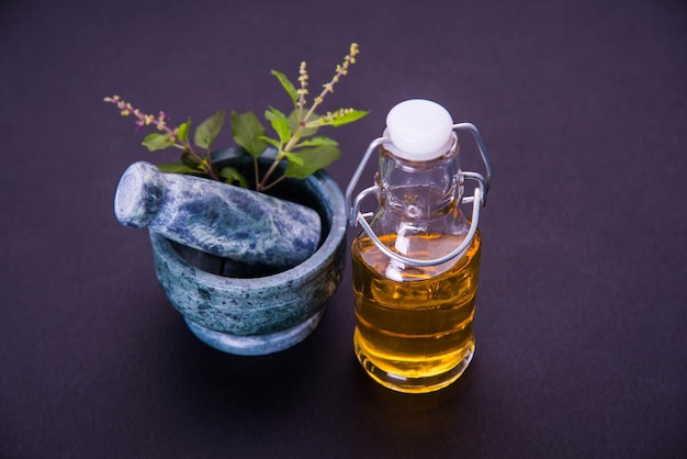 Olio ayurvedico di tulsi, estratto di erbe regina in bottiglia di vetro con rami di basilico santo verde fresco e mortaio con pestello. isolato su sfondo colorato. messa a fuoco selettiva