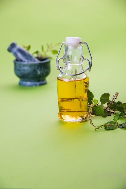 Ayurvedic Tulsi 오일, 유리병에 허브 추출물의 여왕, 신선한 녹색 바질 가지와 페슬이 있는 모르타르. 화려한 배경 위에 절연. 선택적 초점