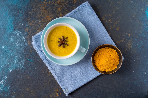 Ayurvedische gouden kurkuma latte melkthee gemaakt met kurkuma en andere kruiden op blauwe achtergrond. Plat liggen.