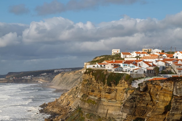 Деревня Азенхас-ду-Мар на вершине утеса с видом на Атлантический океан в муниципалитете Синтра, Португалия.