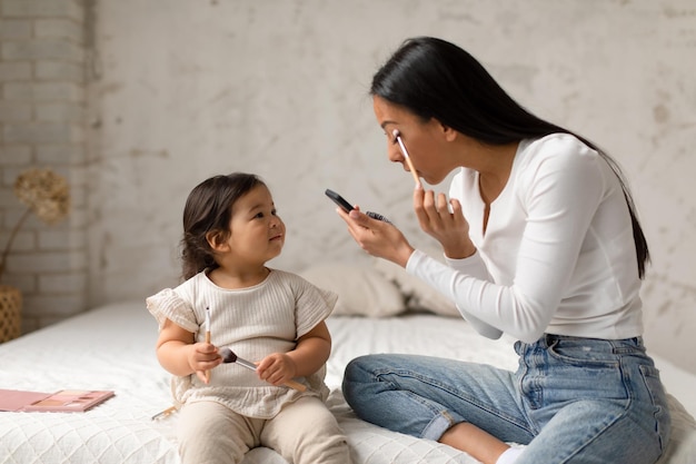 Aziatisch babymeisje dat mama bekijkt die make-up thuis doet