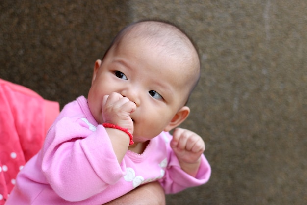 Aziatisch babymeisje dat omhoog zuigend op een vinger kijkt