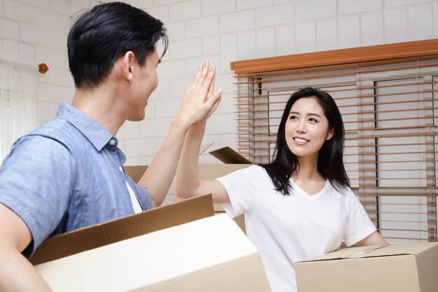 Aziatisch echtpaar koopt een nieuw huis, houdt een kartonnen doos vast om dingen in te stoppen. Verhuis naar een nieuw huis. Concept van het starten van een nieuw leven, het creëren van een gezin.