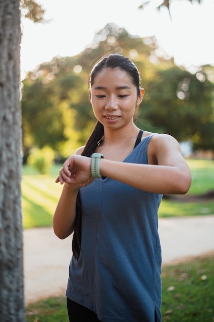 Aziatisch fitnessmeisje dat haar slimme horloge controleert om haar hartslag te zien na het joggen in het park