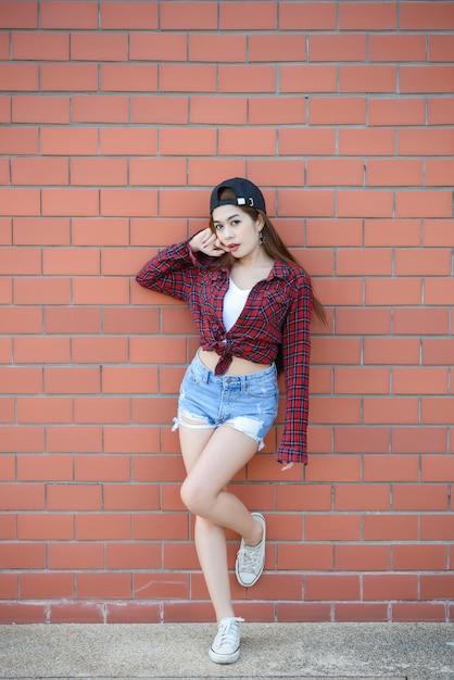 Aziatisch hipstersmeisje op oranje bakstenen muurlevensstijl van moderne tienerGelukkige dame die zich voorneemt fotothailand mensen die geruite overhemden en jeansborrels dragen