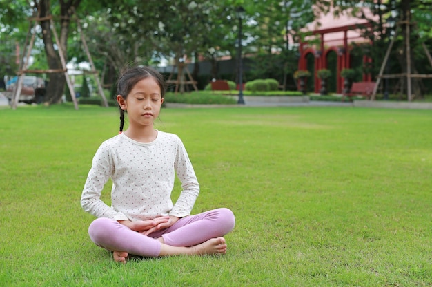 Aziatisch jong meisje dat mindfulness-meditatie beoefent, zittend op het gazon in de tuin vreedzaam concept